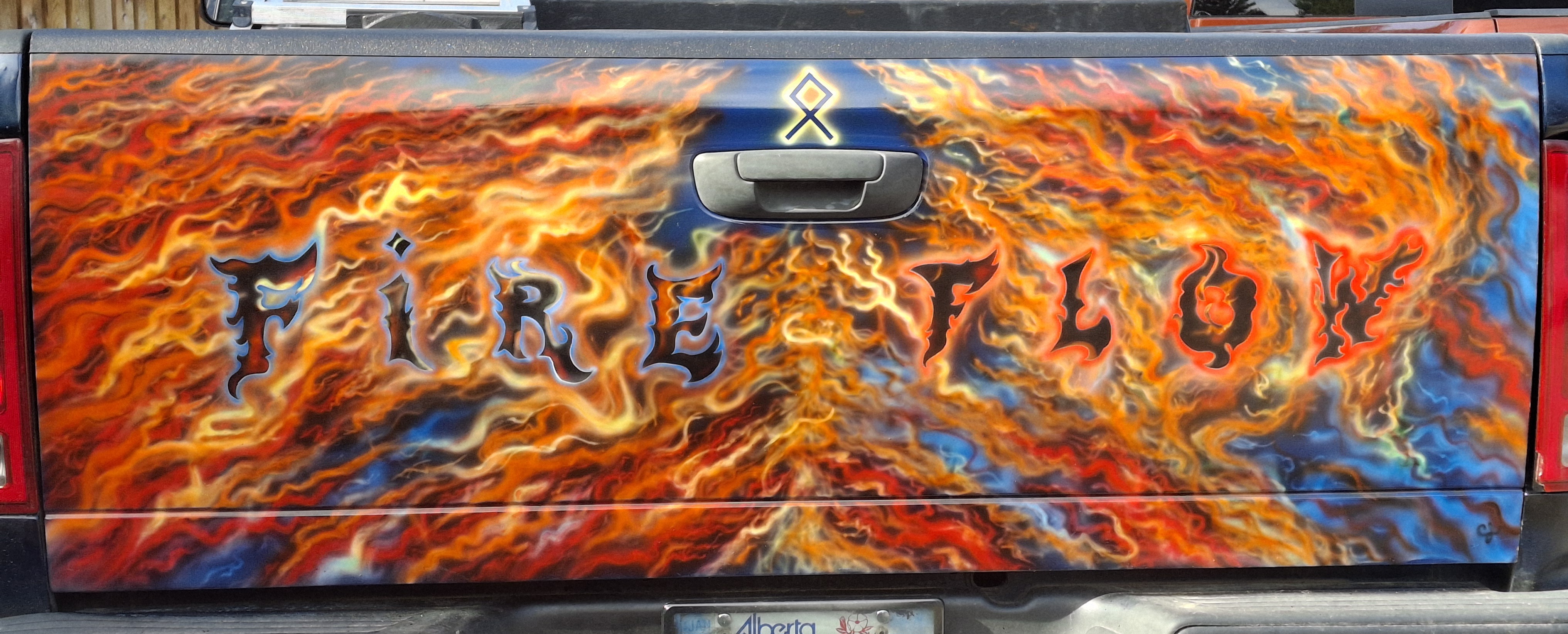 Airbrushed truck tailgate covered in orange and yellow flames with Fire Flow lettering